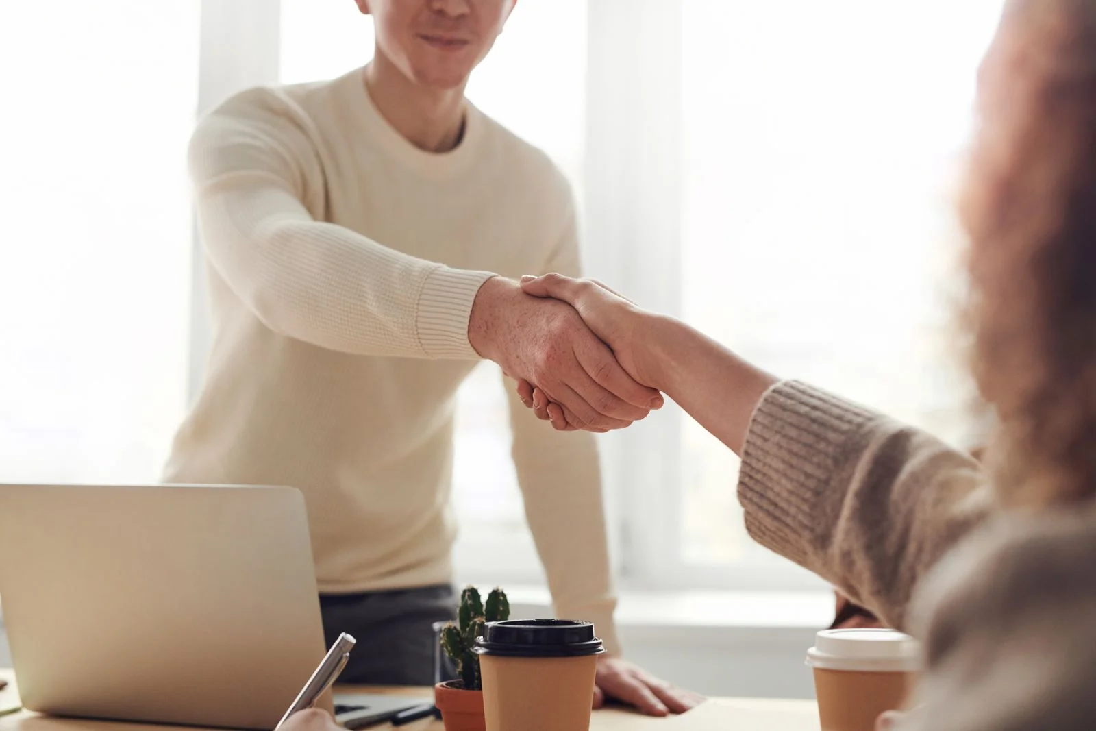 Agency owner shaking hands with a partner at a laptop